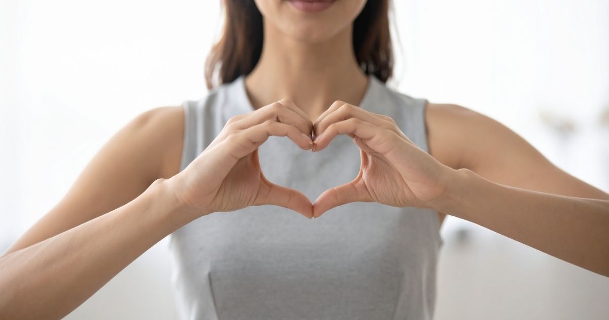 Mulher formando um coração com as mãos na altura do peito, representando cuidados e atenção ao coração da mulher e à saúde cardiovascular.